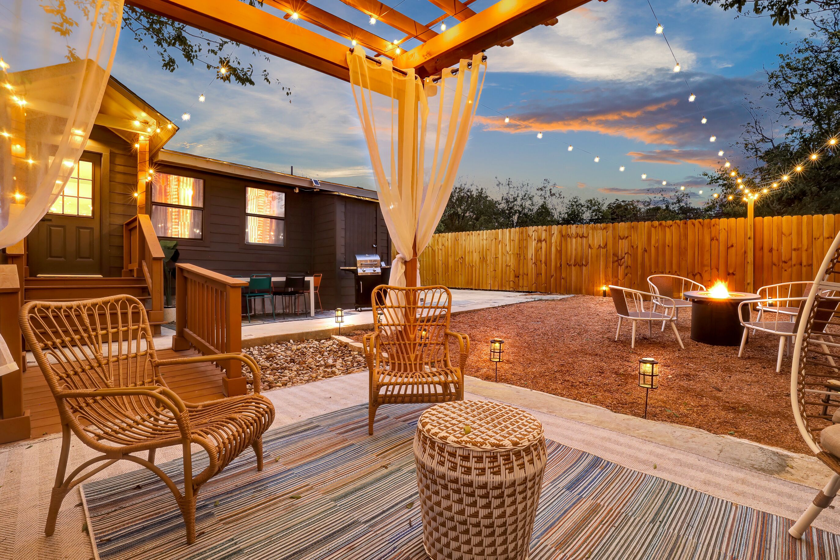 An outdoor patio with wicker furniture, a fire pit, and string lights.