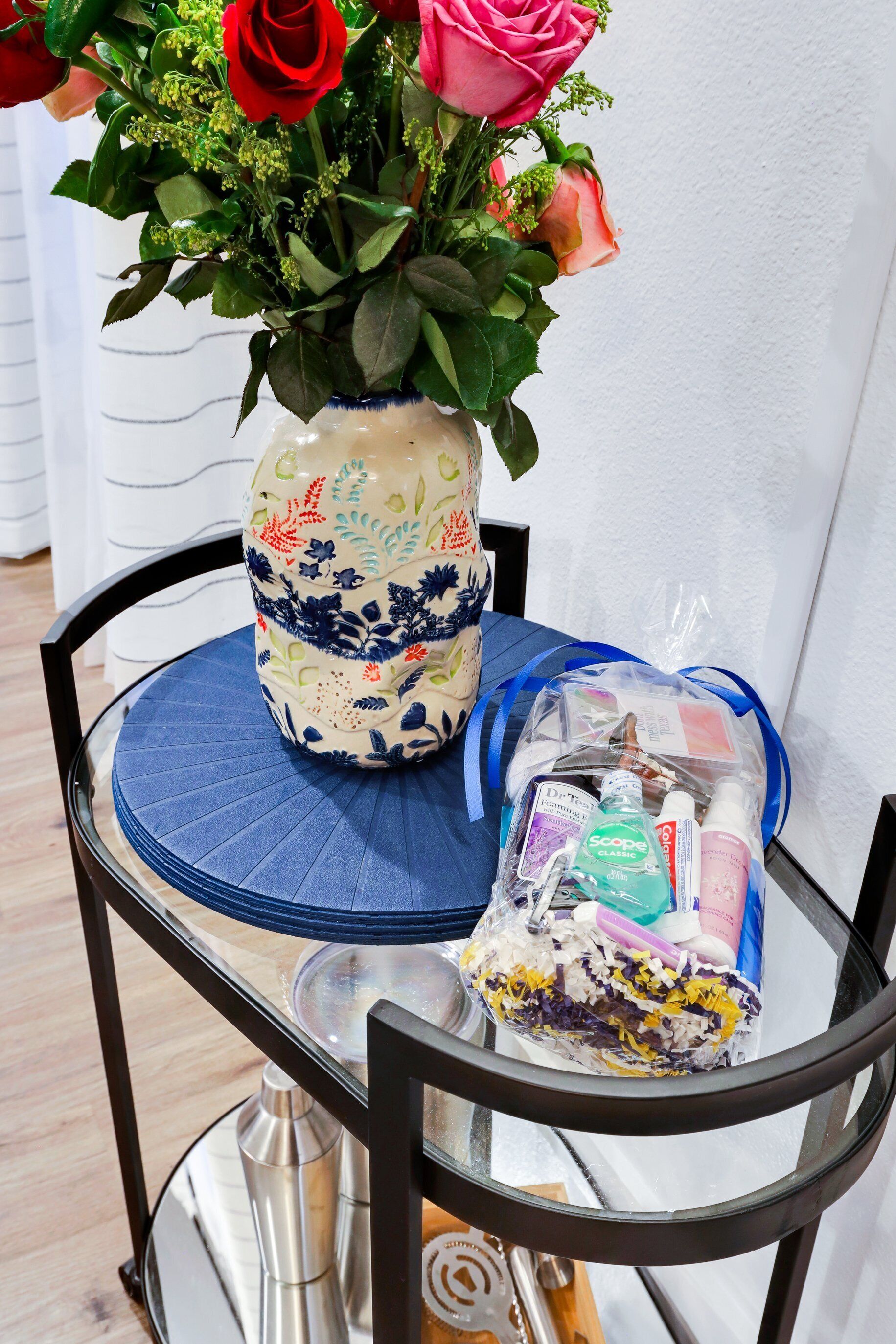 Une table avec un vase de fleurs, un sac cadeau et une bouteille.