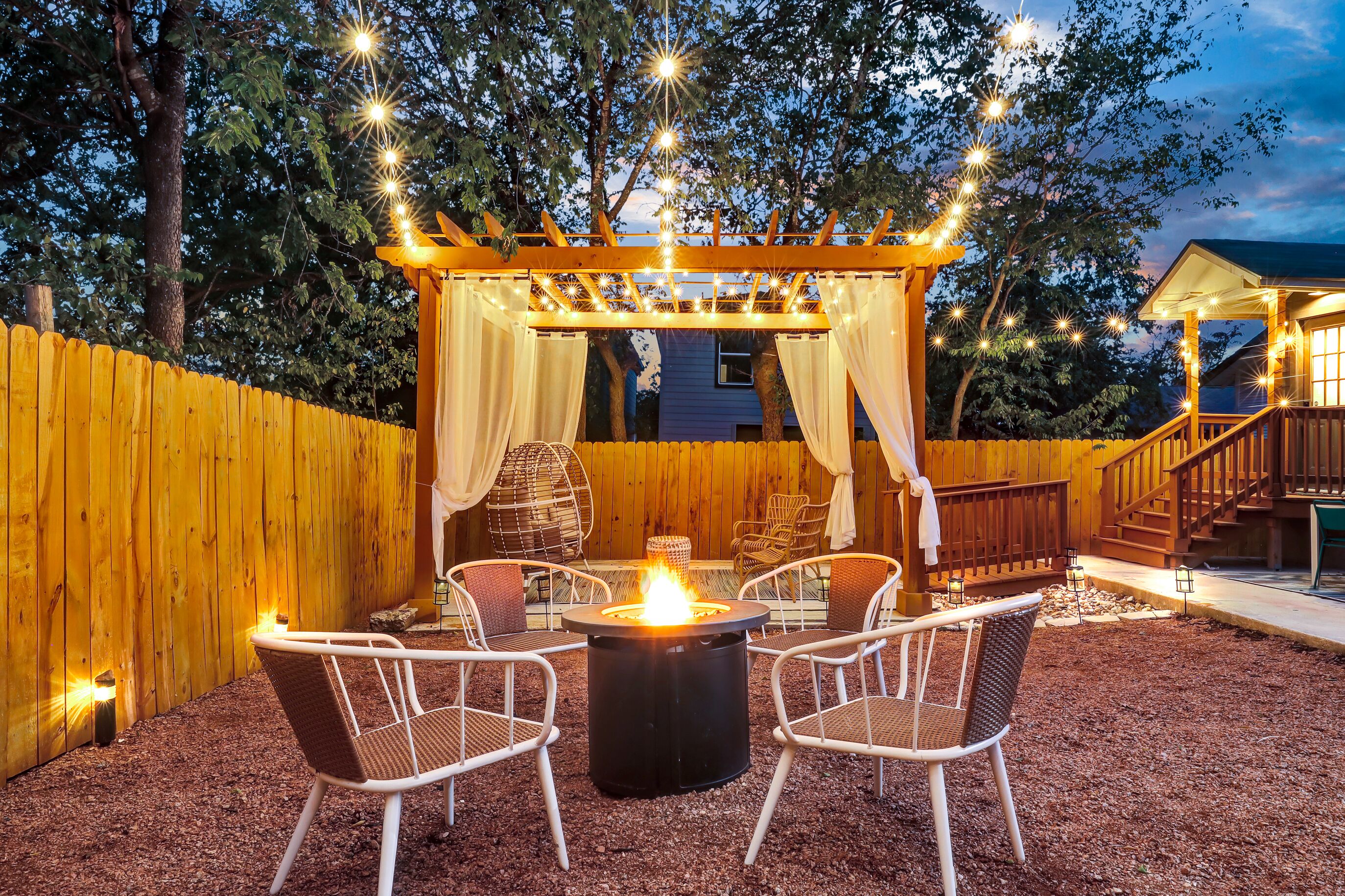 An outdoor patio with a fire pit, wicker chairs, and a pergola with string lights.