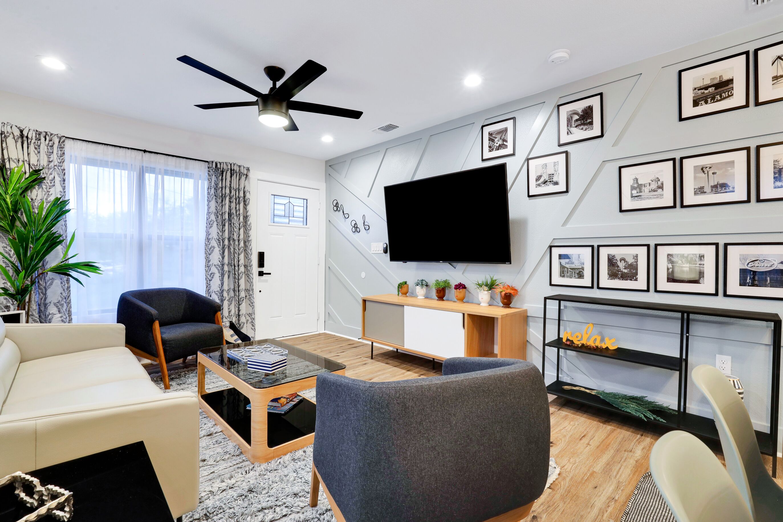 Ein modernes Wohnzimmer mit Flachbildfernseher, Deckenventilator und einer Wand mit gerahmten Bildern.