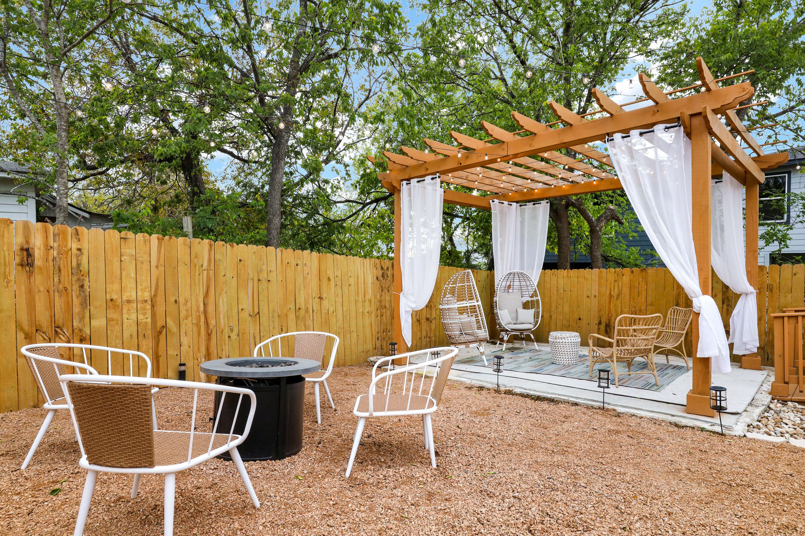 Eine Terrasse im Freien mit einer Pergola, weißen Korbstühlen, einem runden Tisch und einer Glasveranda mit einem Stuhl.