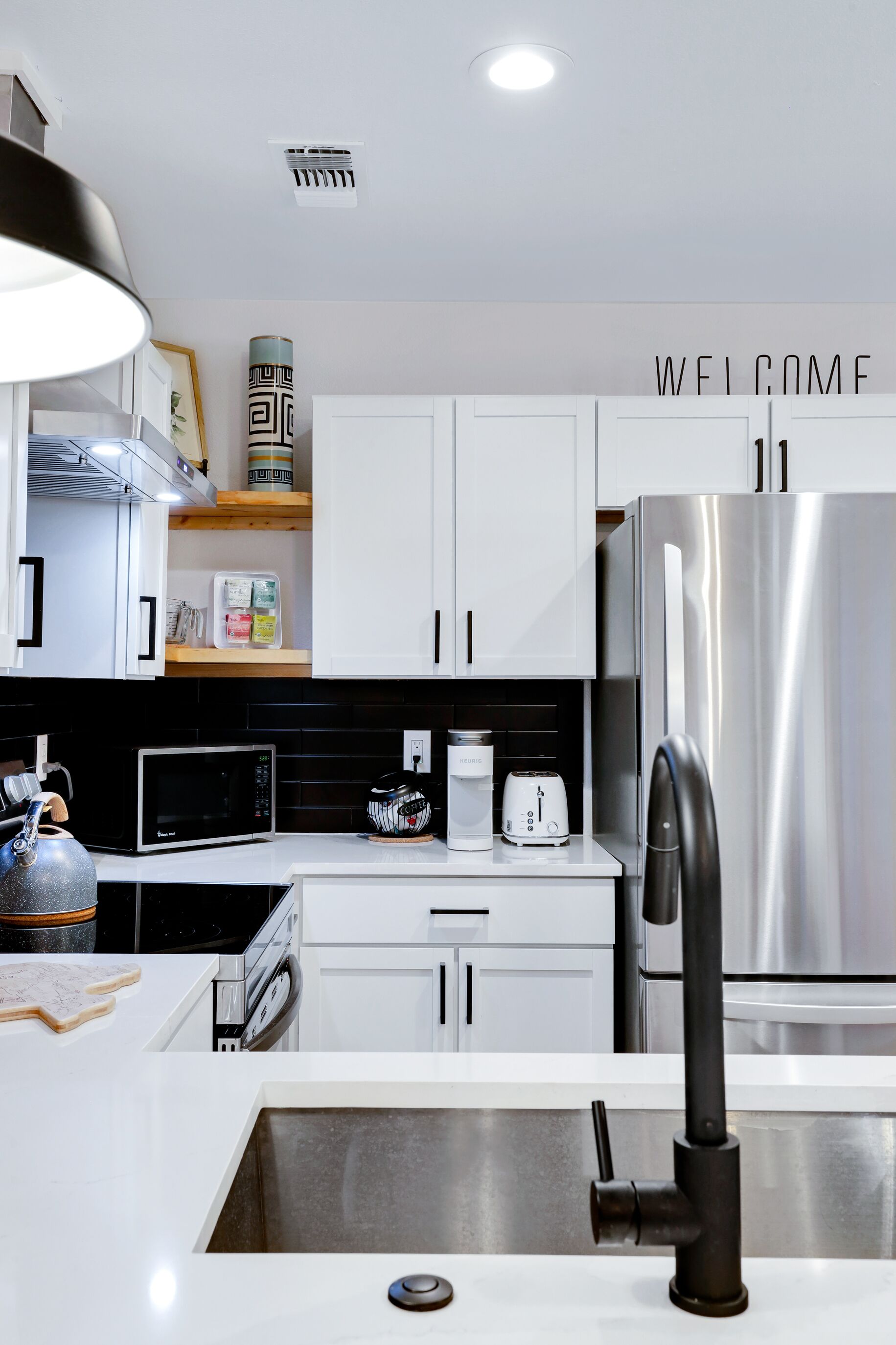 A modern kitchen with white cabinetry, a stainless steel refrigerator, a coffee machine, and a microwave.