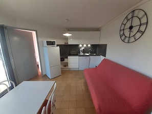 A compact living space with a kitchenette, a dining area, and a red sofa.