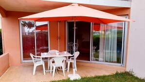 An outdoor patio with a table and chairs, a large umbrella, and a sliding glass door leading to an interior space. - Nice 2 room apt with Pool Richelieu beach Cap d'Agde (LE CAP D AGDE)
