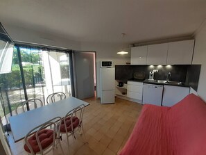 A compact living space with a dining area, kitchenette, and a sliding glass door leading to an outdoor area. - Nice 2 room apt with Pool Richelieu beach Cap d'Agde (LE CAP D AGDE)