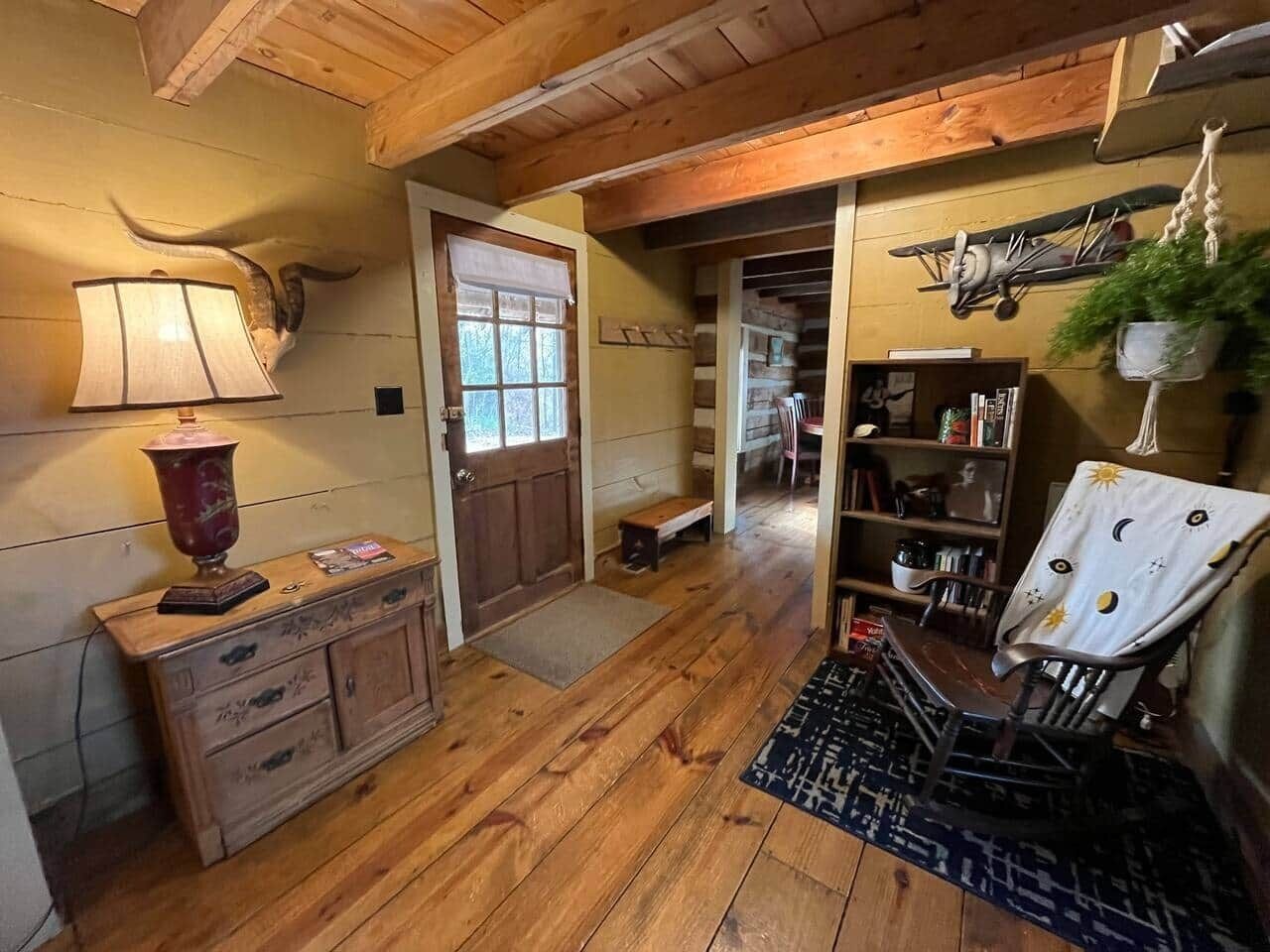 A rustic wooden interior with a wooden cabinet, a lamp, a bench, and a chair with a sun-patterned cover.