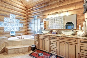 A log cabin bathroom with a bathtub, two sinks, and a large mirror.