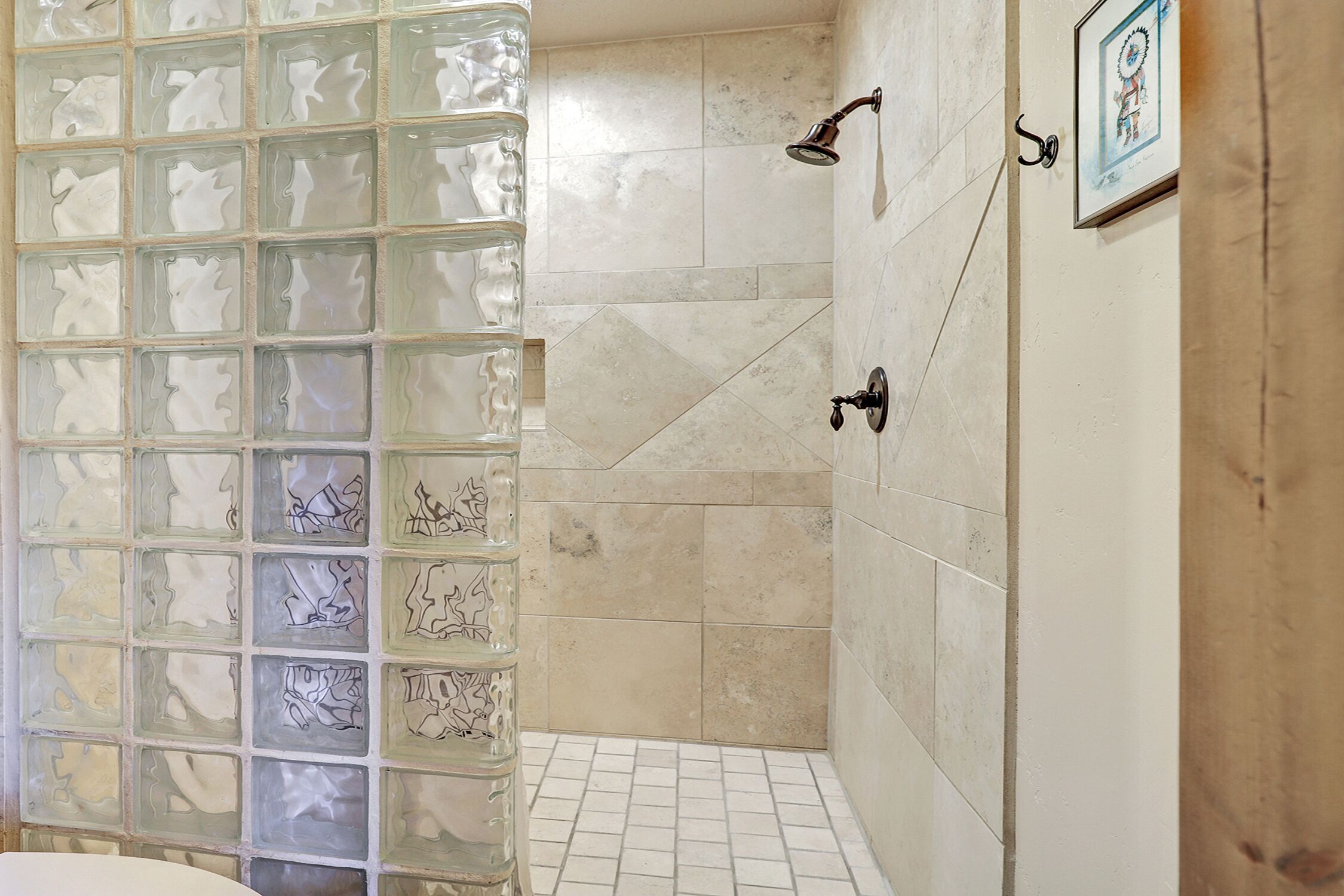 A bathroom with a glass shower enclosure, tiled walls, and a framed picture on the wall.