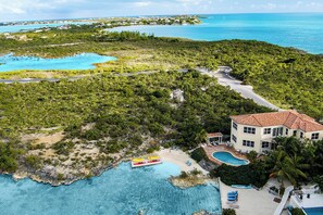 Vista aérea de una propiedad costera con una casa grande, una piscina y un área de playa con kayaks.