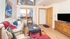 A living room with a sofa, coffee table, TV, and a large window with a view of mountains. - Cimarron Slopeside Retreat  Ski In/Ski Out (Telluride)