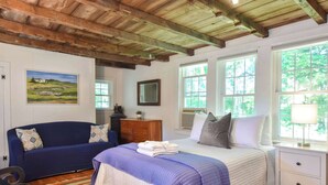 A bedroom with a bed, a blue sofa, a dresser, and a window with a view of trees. - Private Downtown Wellfleet Location! (Wellfleet)