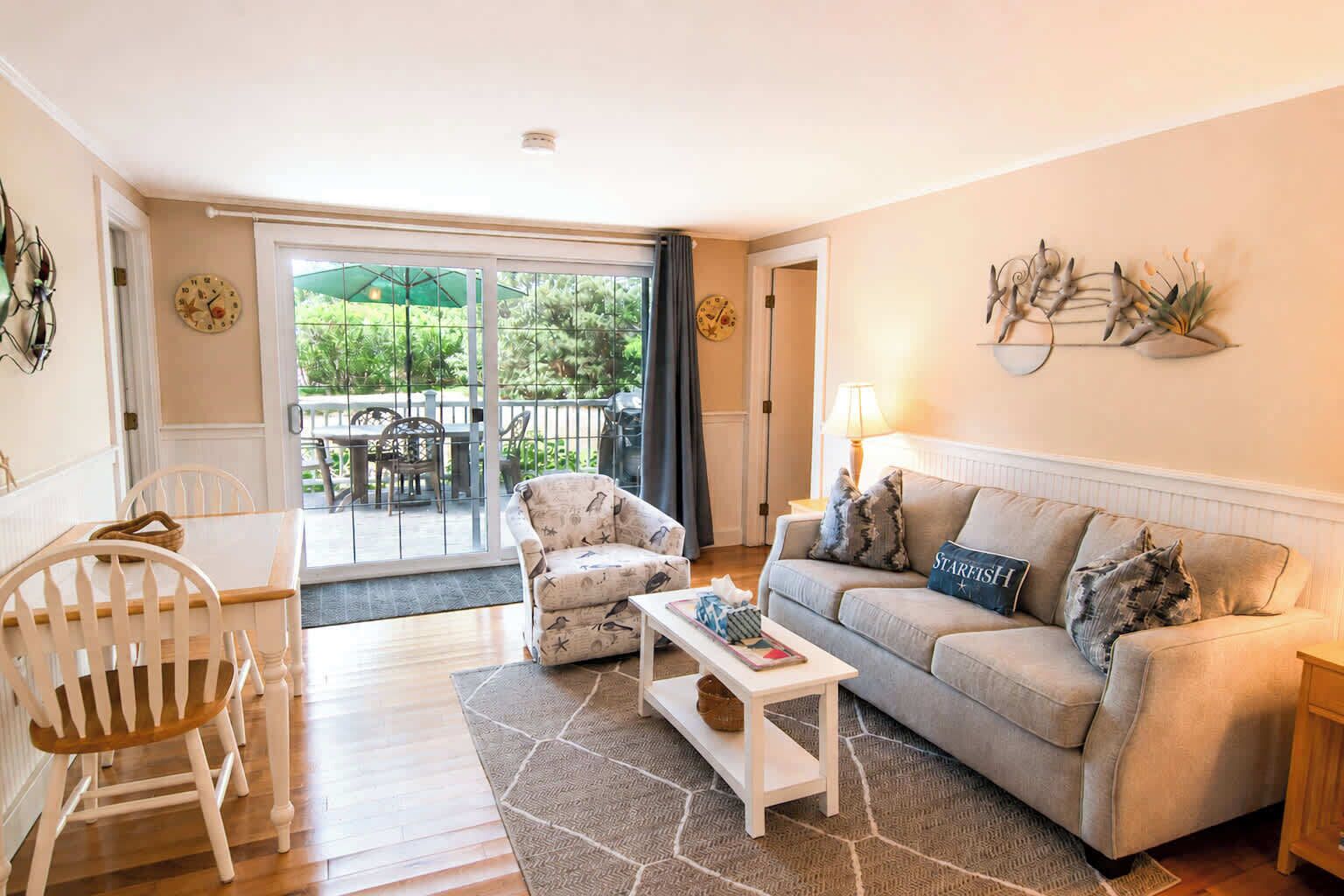 A living room with a sofa, armchair, coffee table, and a dining area with chairs and a table.