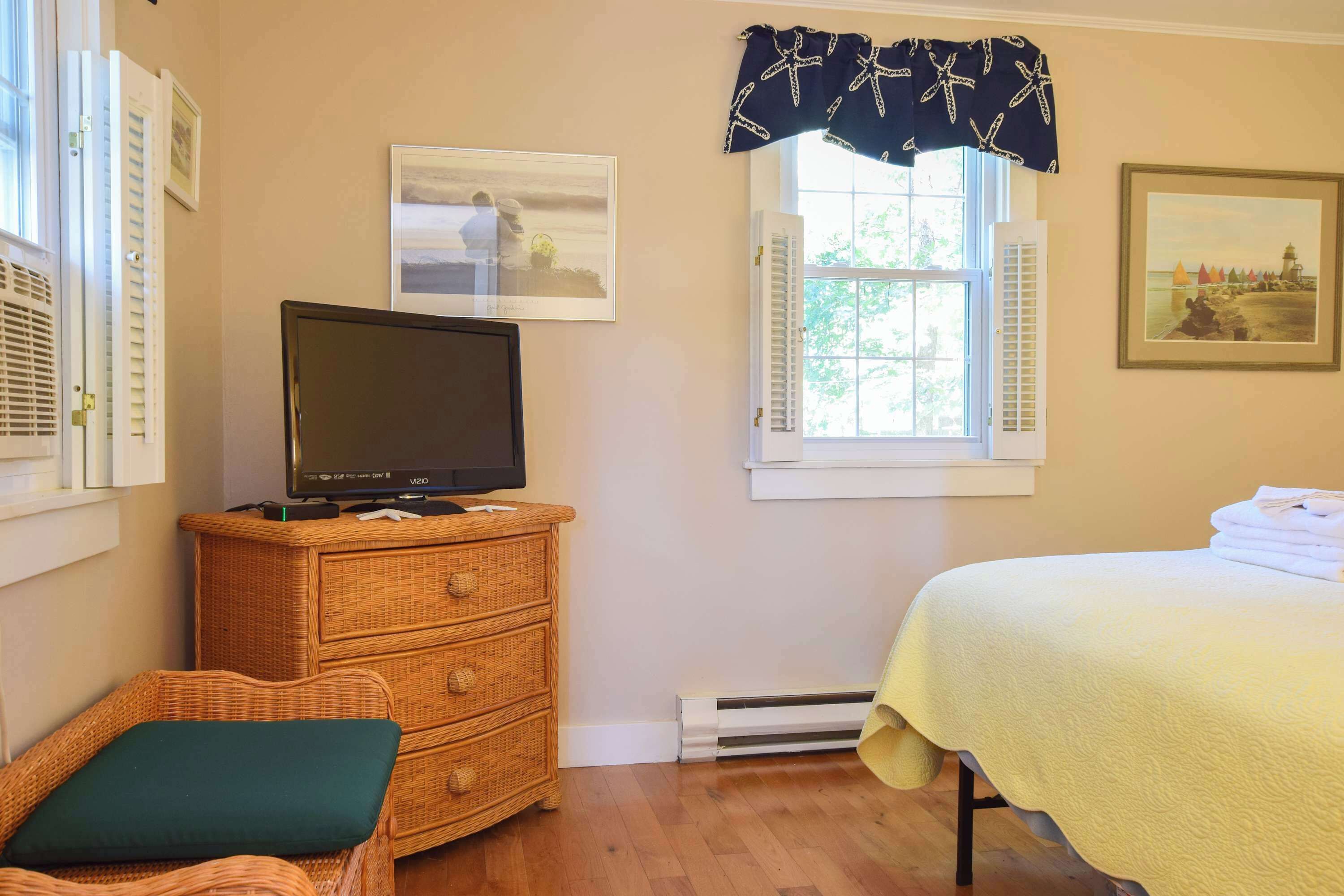 A bedroom with a bed, a television on a dresser, a window with shutters, and wall-mounted pictures.