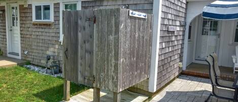 A wooden outdoor shower enclosure in a residential backyard with a patio and a chair.