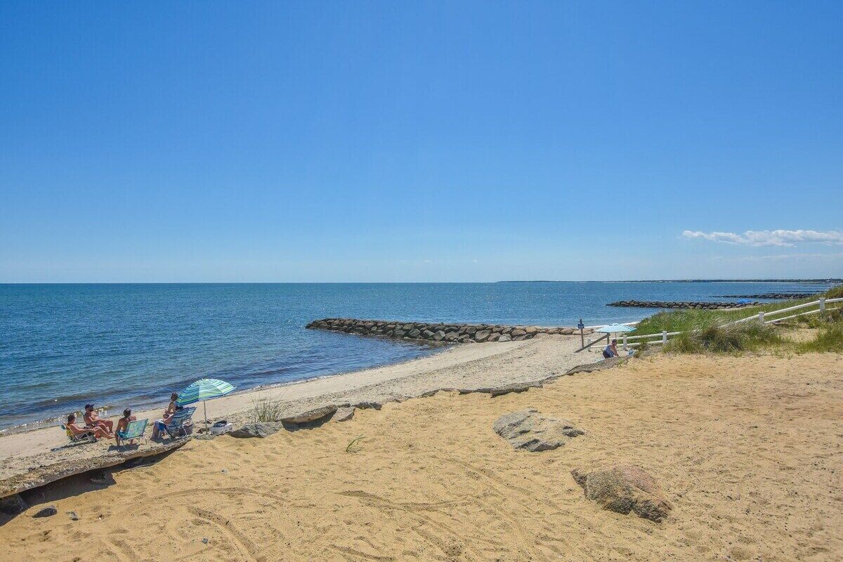 A beach with a clear sky, a sandy shore, and a few people relaxing under umbrellas.