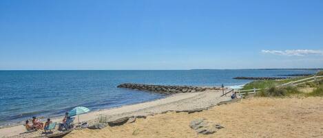 A beach with a clear sky, a sandy shore, and a few people relaxing under umbrellas.