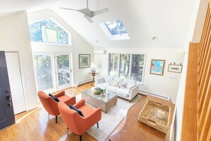 A spacious living room with a high ceiling, large windows, and a ceiling fan.
