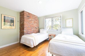A room with two beds, a brick fireplace, and a window with a view of trees.