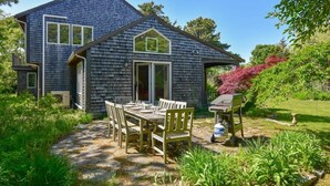 Une maison avec un patio en pierre, une table à manger avec des chaises et un barbecue.