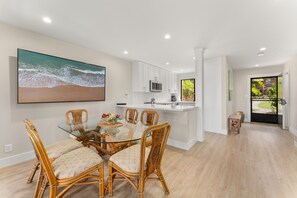 A modern kitchen with white cabinets, a central island, and a dining area with wicker chairs and a glass table.