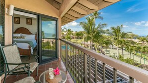 A balcony with a bed, a chair, and a table with a flower. - Beautifully remodeled ocean view condo in Wailea WE27B (Kihei)