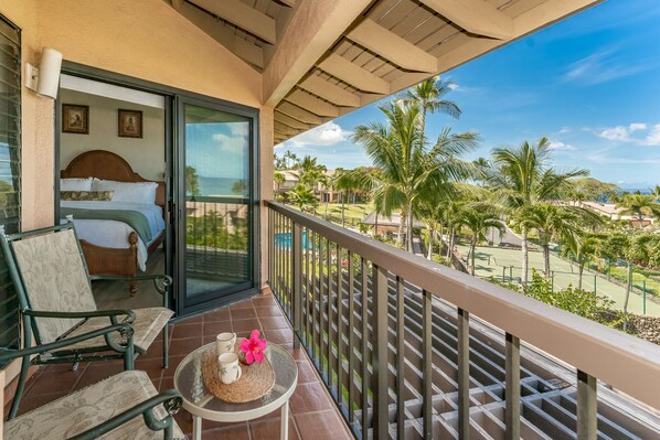 A balcony with a bed, a chair, and a table with a flower.