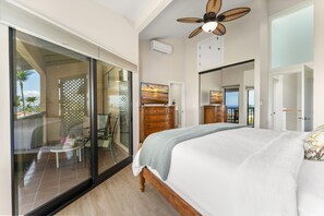 A bedroom with a large bed, a ceiling fan, a wooden dresser, and a sliding glass door leading to a balcony.