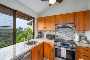Enjoy a serene atmosphere with a view of lush greenery from the large window in this kitchen.