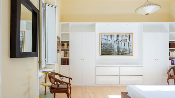 Una camera da letto con un letto, una sedia, una scrivania, una libreria e un quadro appeso al muro.