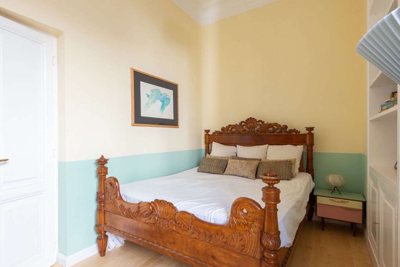 Een slaapkamer met een houten bed, nachtkastje en een foto in een lijst aan de muur.