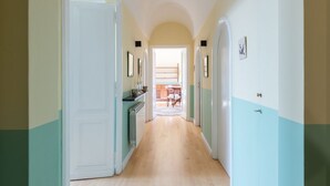 Un corridoio con pavimento in legno, porte bianche e vista su una sala da pranzo.