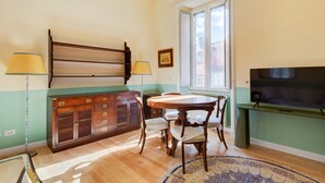 Zona pranzo con tavolo e sedie in legno, un mobile contenitore con cassetti, televisione su un mobile basso e una finestra con vista.