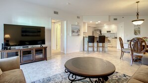 A modern living room with a TV, sofa, and dining area. - Oceanwalk 2BR | Fountain Views, Private Balcony & 5-Min Walk to Beach (New Smyrna Beach)