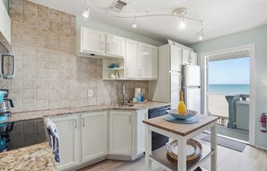A kitchen with white cabinets, a granite countertop, and a view of the beach.