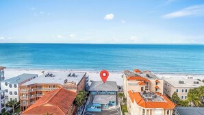 A coastal hotel with a red location marker, beachfront balconies, and a view of the ocean.