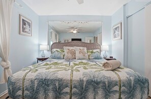 Quarto com cama, ventilador de teto, espelho grande e janela.