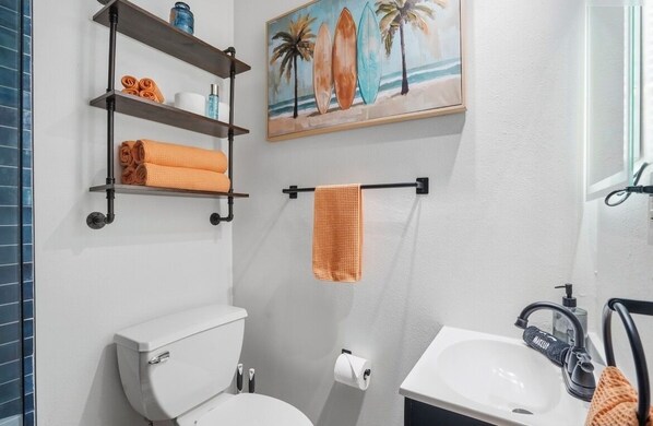 Une salle de bain équipée de toilettes, d’un lavabo, d’un porte-serviettes et d’étagères où sont rangées les serviettes.