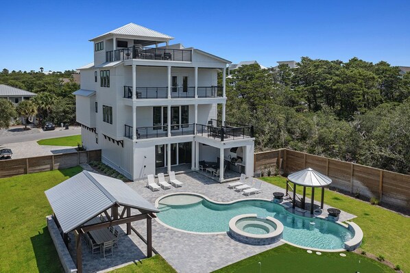 Une maison à deux étages dotée d’une piscine, d’un espace extérieur aménagé pour se détendre et d’un patio couvert.