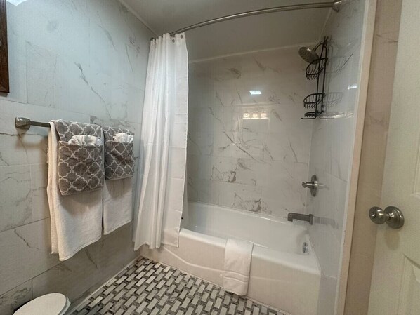 Et badeværelse med bruser, toilet og et håndklædestativ med håndklæder.