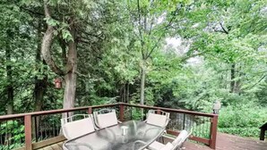 Une terrasse en bois avec une table à plateau de verre et des chaises blanches dotées de coussins.