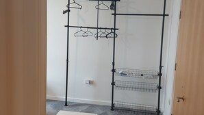 Una habitación con pared blanca, una estantería de metal negro con perchas, una mesa blanca y una puerta de madera.