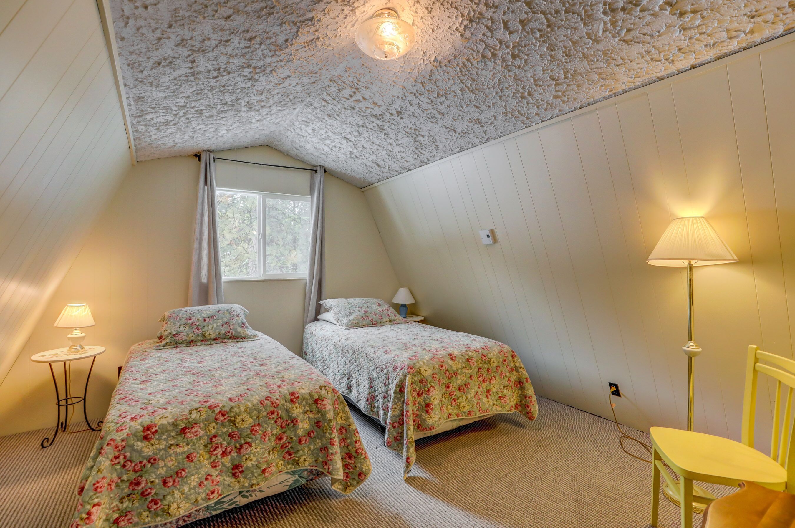 A bedroom with two beds, a window, a lamp, and a ceiling light.