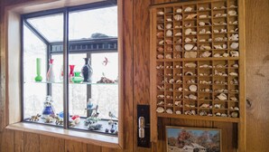 Una habitación con una ventana que muestra varios objetos decorativos y un mueble de madera lleno de conchas marinas.