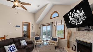 Un salón amplio con techo alto, chimenea y un televisor que muestra 'Coastal Carolina Vacations and Sales'.