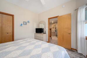 Une chambre à coucher comprenant un lit, une commode, un téléviseur et une porte donnant sur une salle de bain.