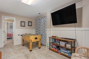A room with a foosball table, a flat-screen TV, and a bookshelf with board games. - The Purple Dandelion-Oceanside,dog-friendly 🐶easy beach access,community pool (Corolla)