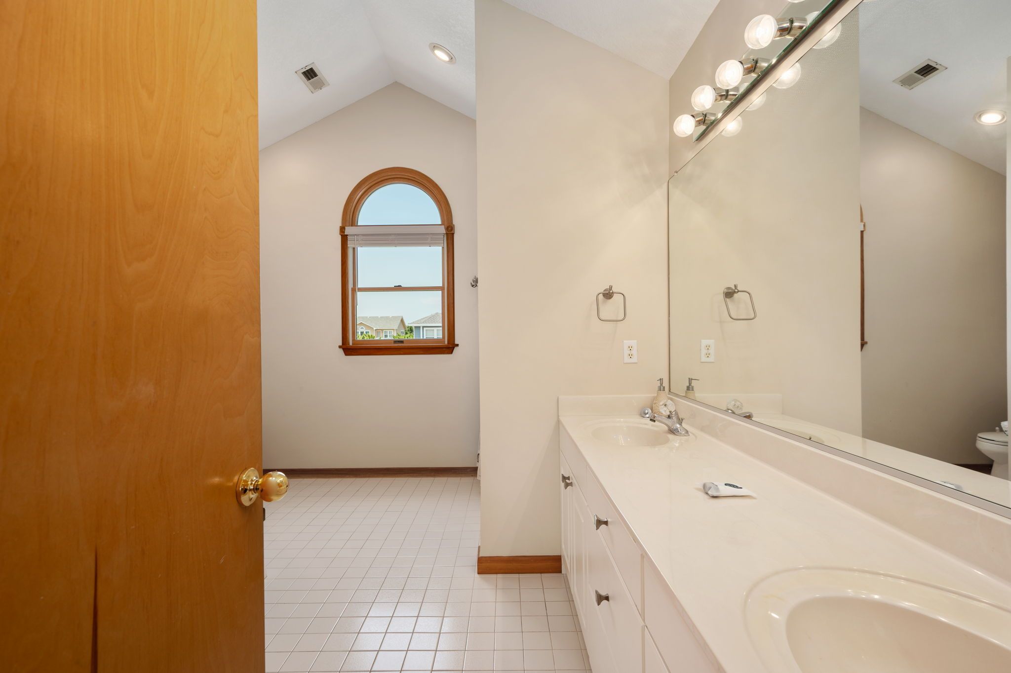A bathroom with a large mirror, a sink, and a window.