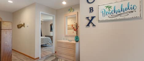 A hallway with a wooden door, a mirror, a dresser, and a wall sign reading "BOX Beachaholic".