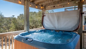 Terraza de madera con jacuzzi, luces colgantes y vistas a árboles.
