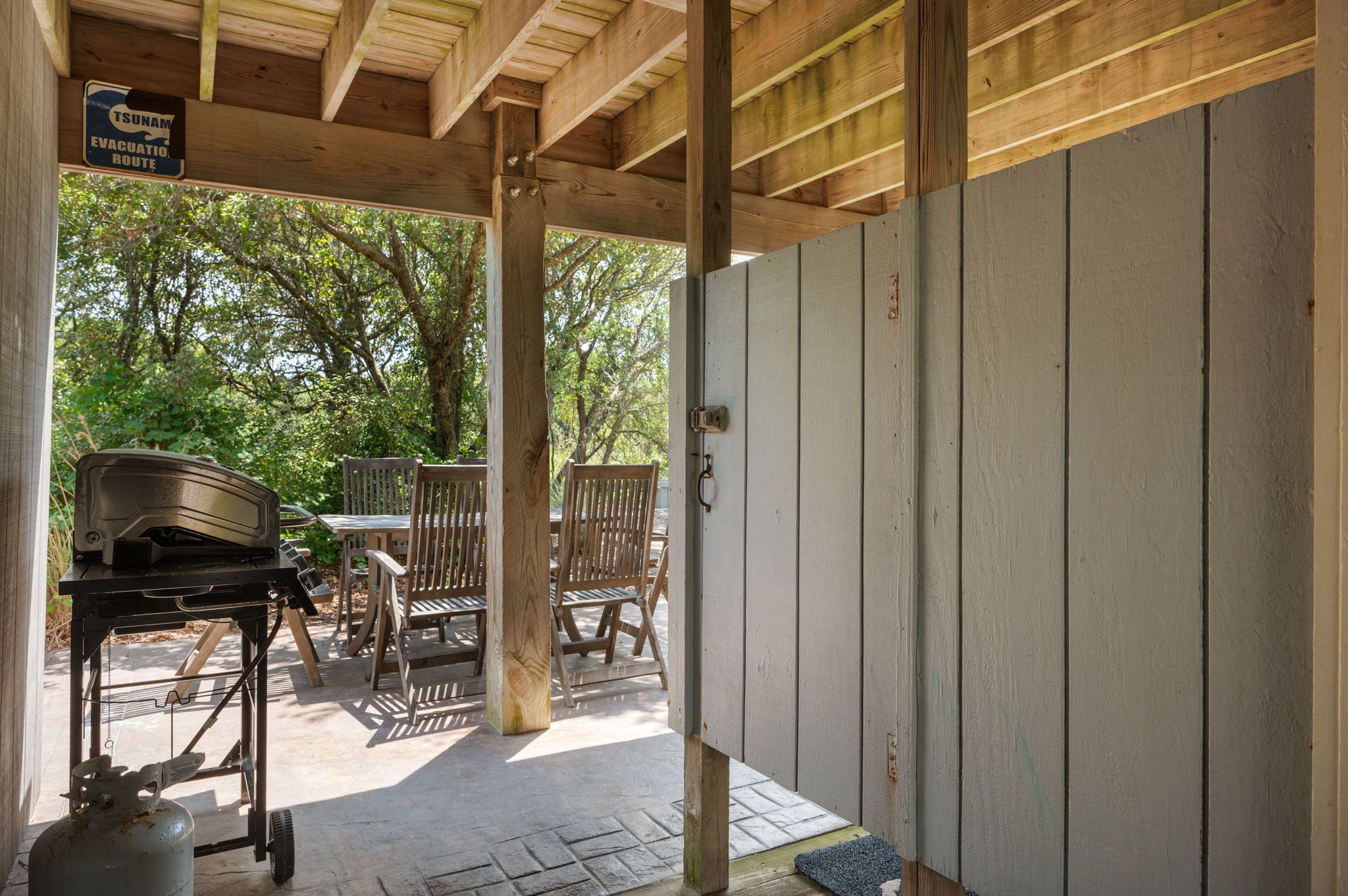 An outdoor patio area with a grill and chairs, a gas canister, and a sign indicating a tsunami evacuation route.
